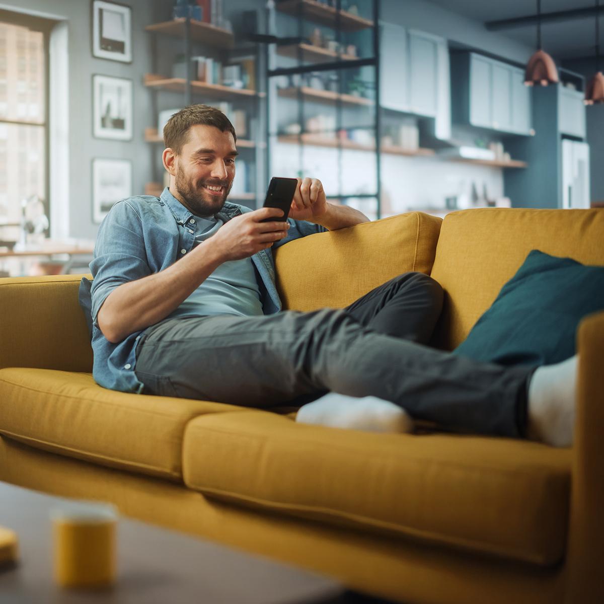 Mann mit Handy auf Sofa liegend