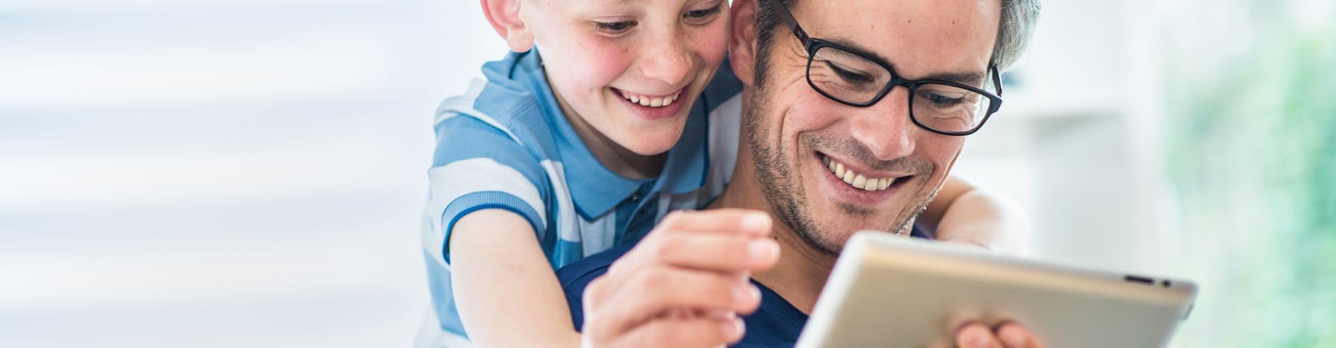 Vater und Sohn nutzen gemeinsam Tablet auf dem Sofa. Digitaler Kundenservice der Stadtwerke Witten für Strom- und Gas-Anliegen ohne Registrierung