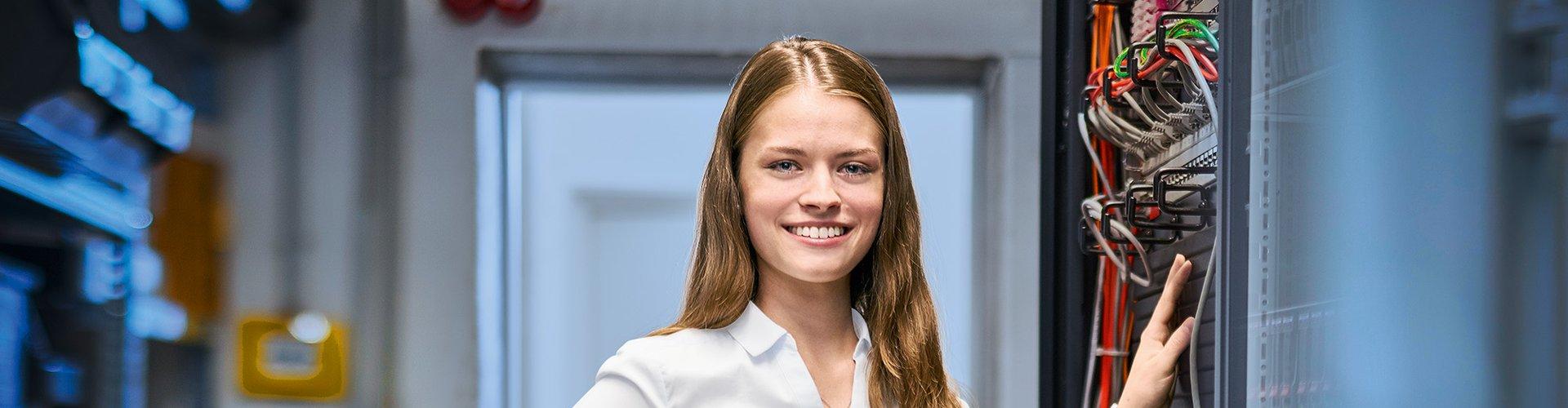 Frau steht mit Kabel in der Hand an einem Serverschrank in dem Patchkabel stecken.