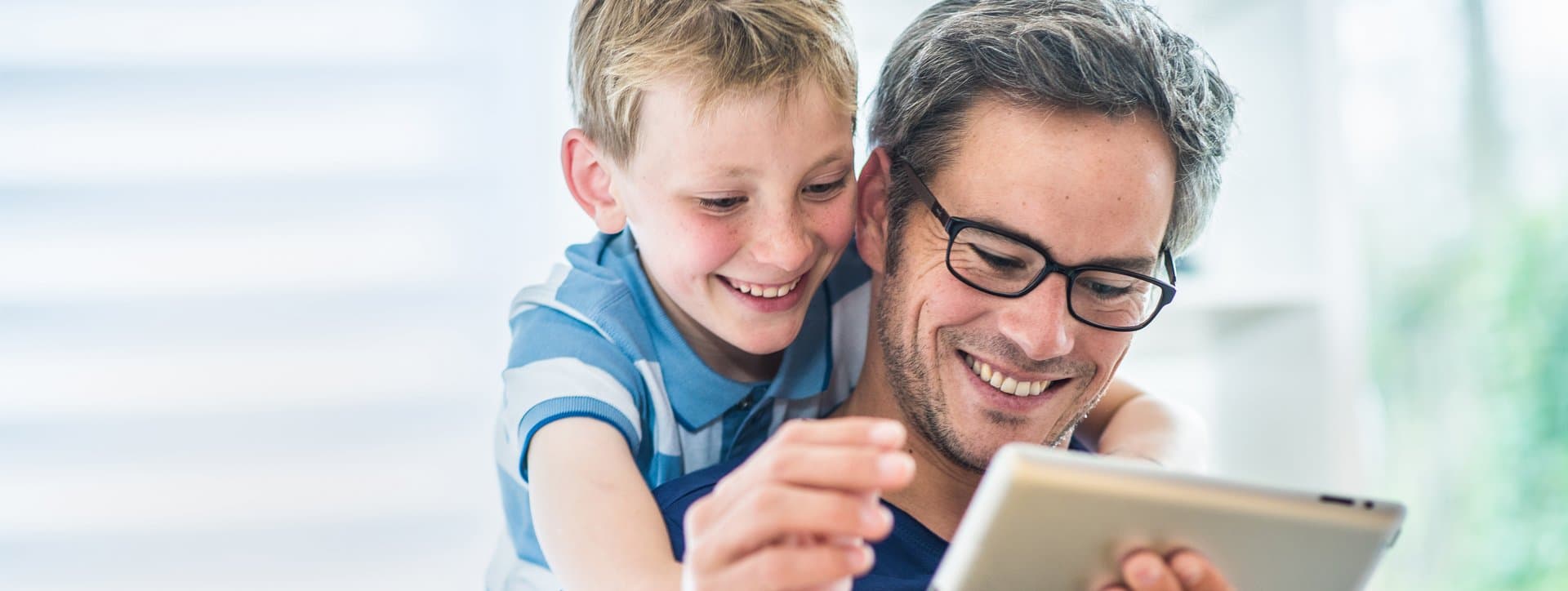 Vater und Sohn nutzen gemeinsam Tablet auf dem Sofa. Digitaler Kundenservice der Stadtwerke Witten für Strom- und Gas-Anliegen ohne Registrierung