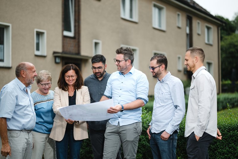 Projektteam für das Quartierskonzept steht vor einem Wohngebäude. Foto: Ludgar Staudinger
